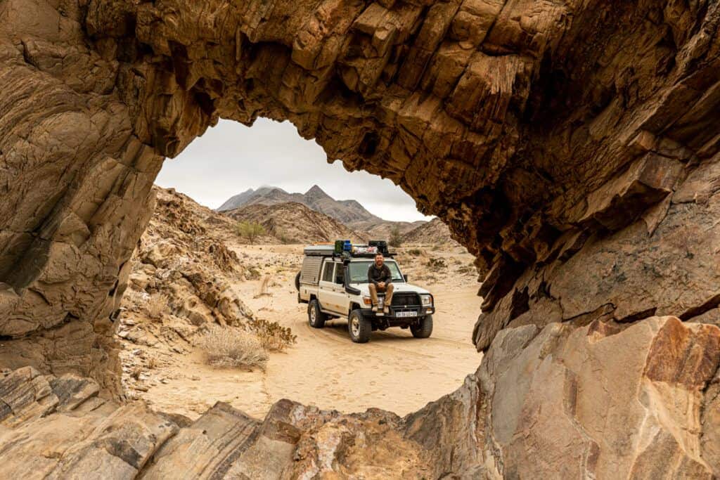 A 4x4 framed by a circular rock arch in Namibia